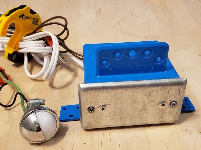 A Blue Box tester: a blue electrical box with a metal cover plate, a small lamp and test leads.
